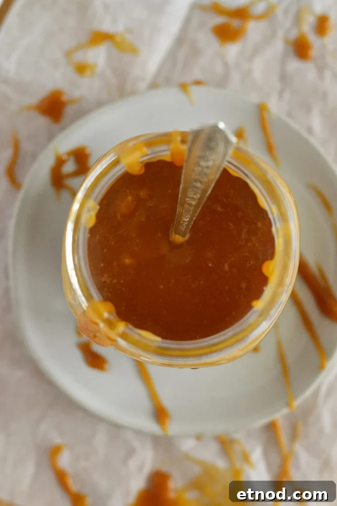 Creamy Cookie Butter Caramel Sauce Recipe 3 looking down into a jar of caramel sauce with a spoon sticking out the top