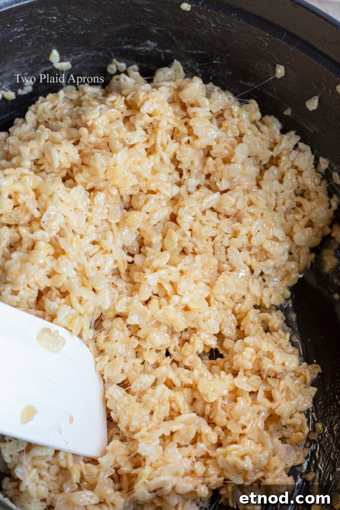 Stirring Rice Krispies cereal with melted butter and marshmallows in a pot.