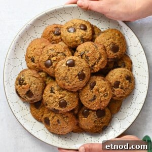 Soft Banana Chocolate Chip Cookies — Paleo Grain-Free Recipe 18 An overhead shot of two hands holding a white plate piled high with paleo banana chocolate chip cookies.