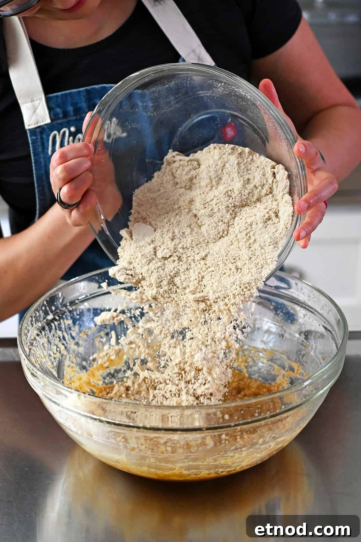 Soft Banana Chocolate Chip Cookies — Paleo Grain-Free Recipe 8 Adding the bowl of dry ingredients to the glass mixing bowl of wet ingredients to make paleo banana cookies.
