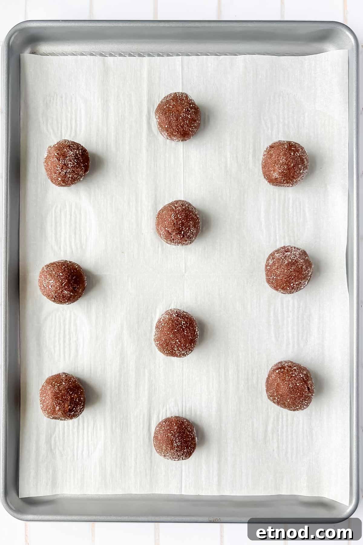 Chocolate Peppermint Kiss Cookies Recipe for Holiday Baking 8 chocolate peppermint kiss cookie dough balls aligned on silver baking tray lined with parchment.