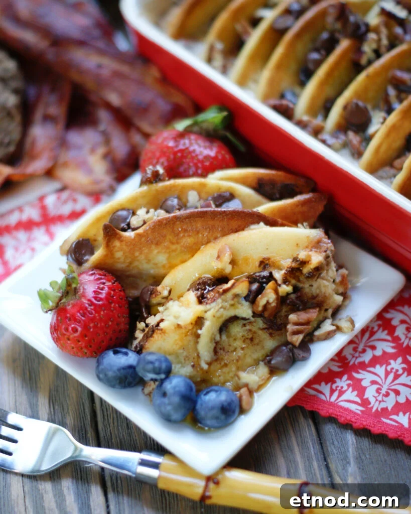 A plate of chocolate chip pancake casserole with maple syrup, blueberries and strawberries to show how to serve this breakfast recipe.