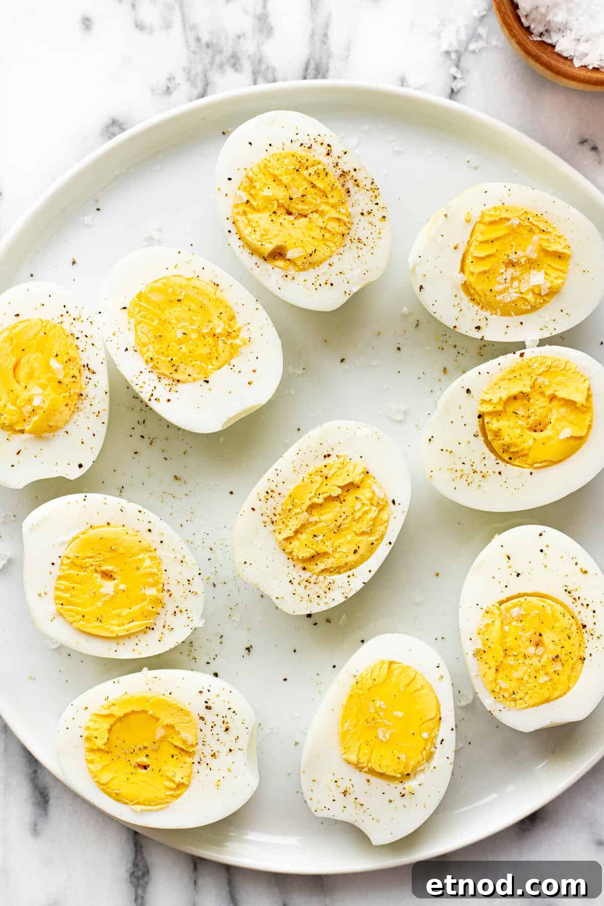 White plate with sliced hard boiled eggs garnished with salt and pepper.