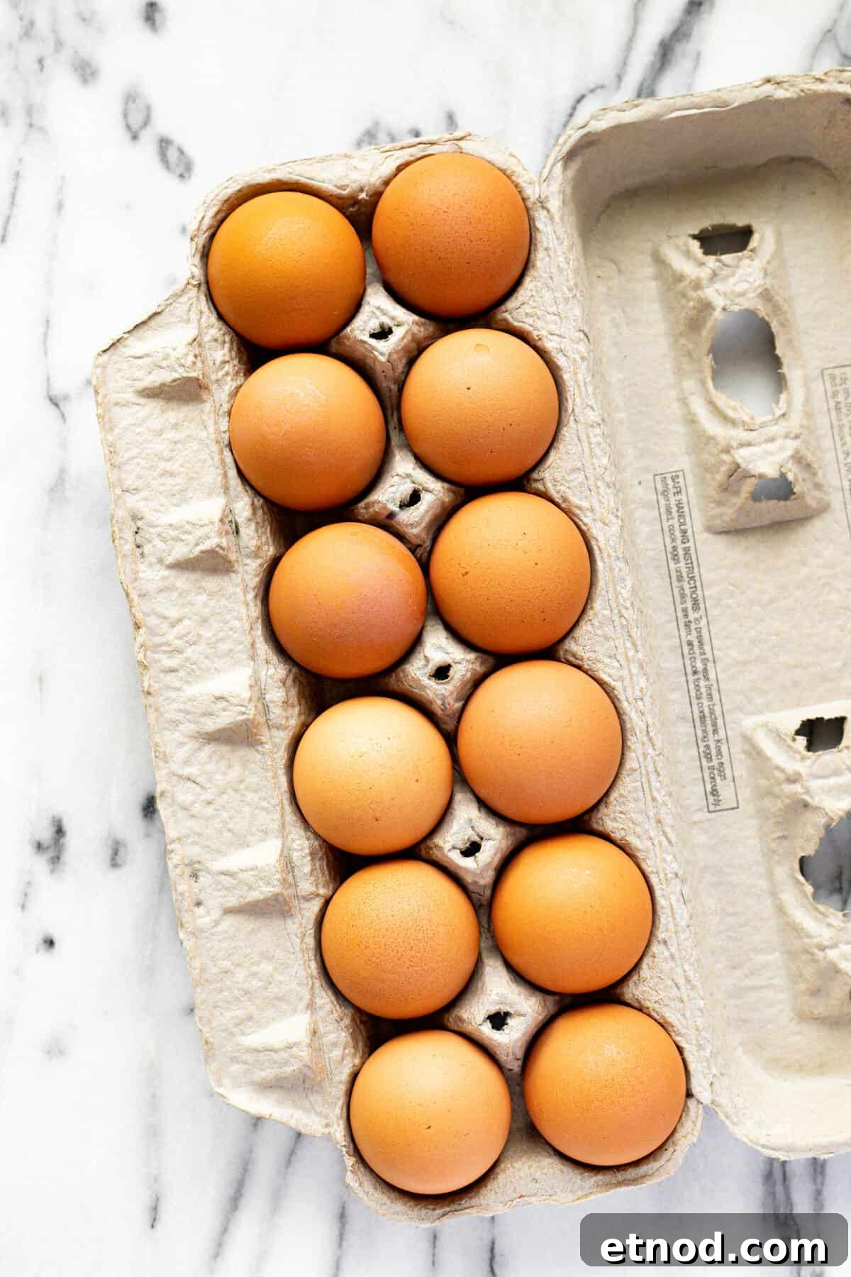 A carton of brown eggs on a white marble counter top.