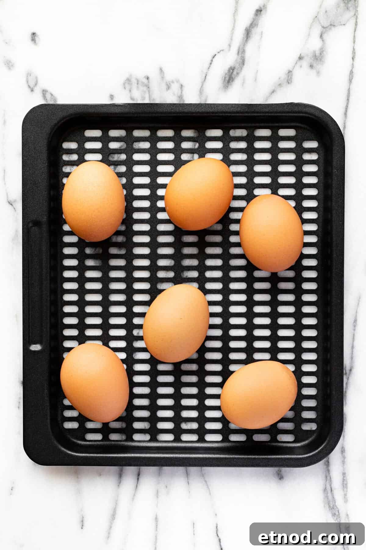 Black air fryer tray with brown eggs on it.