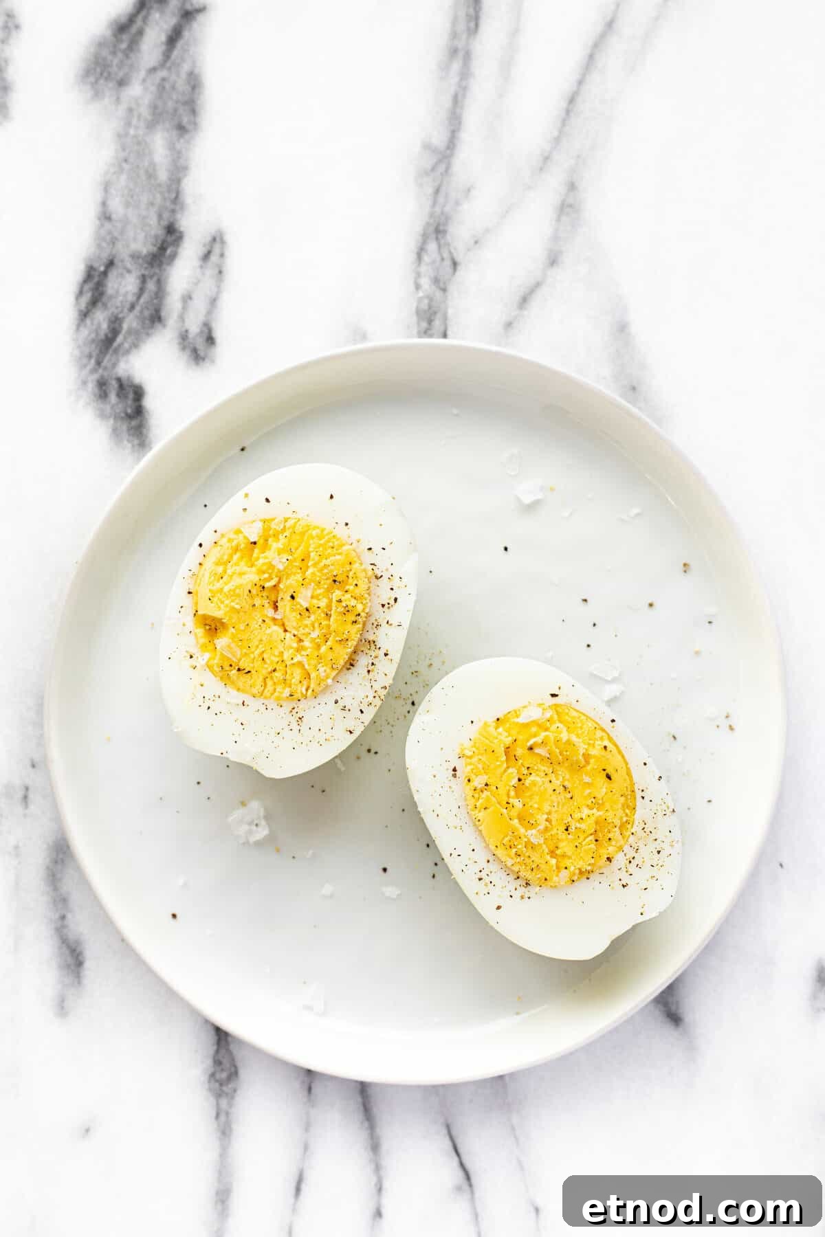 White plate with sliced hard boiled eggs garnished with salt and pepper.