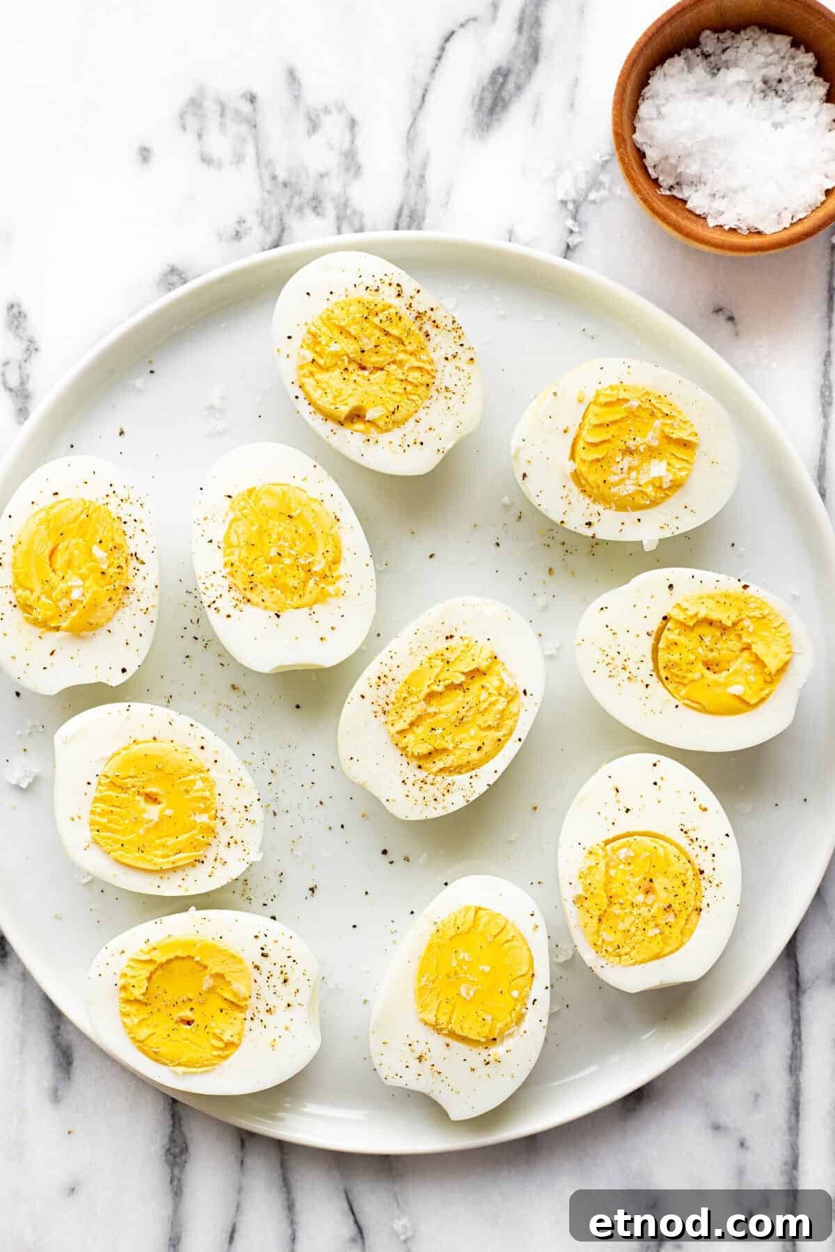 White plate with sliced hard boiled eggs garnished with salt and pepper.
