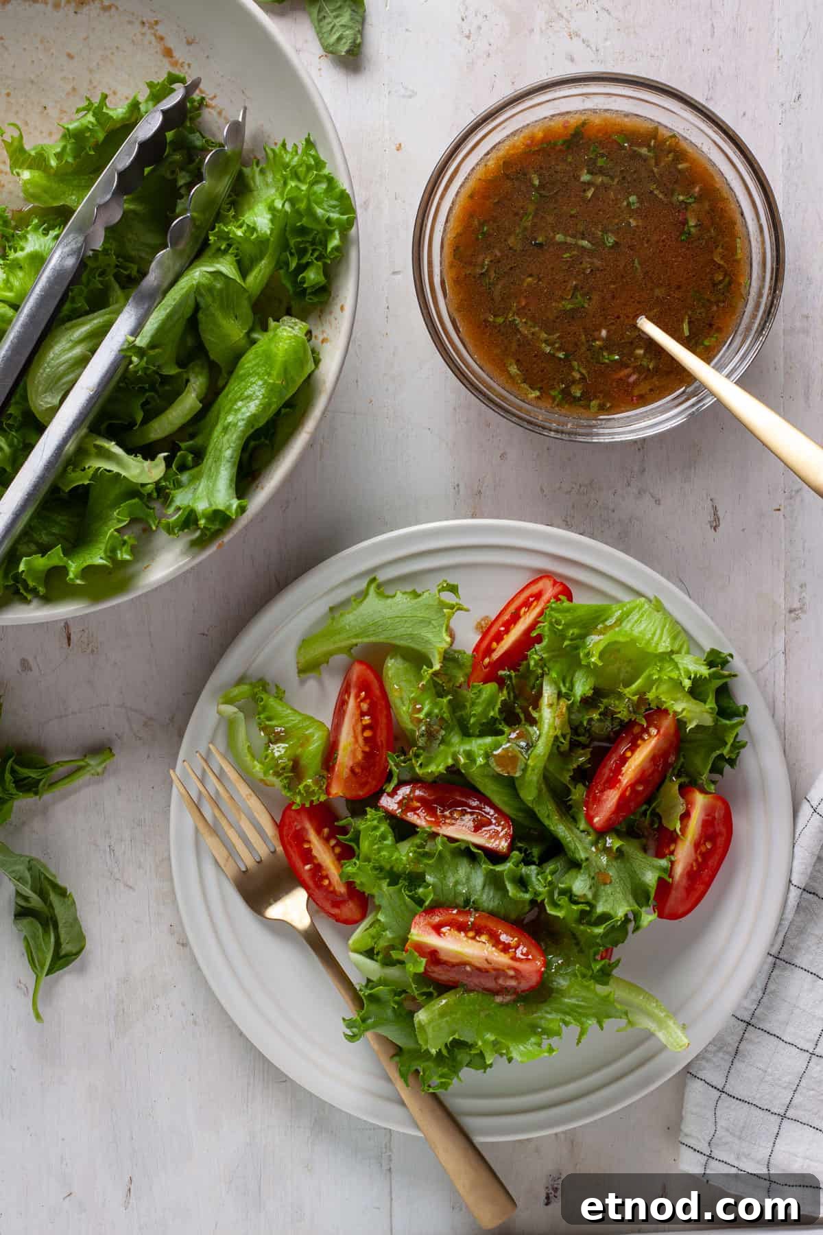 A simple side salad with greens and tomatoes with basil balsamic vinaigrette to the side.