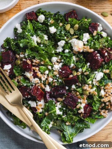 A serving bowl of beet and kale salad with farro and crumbled feta on a butcherblock counter.