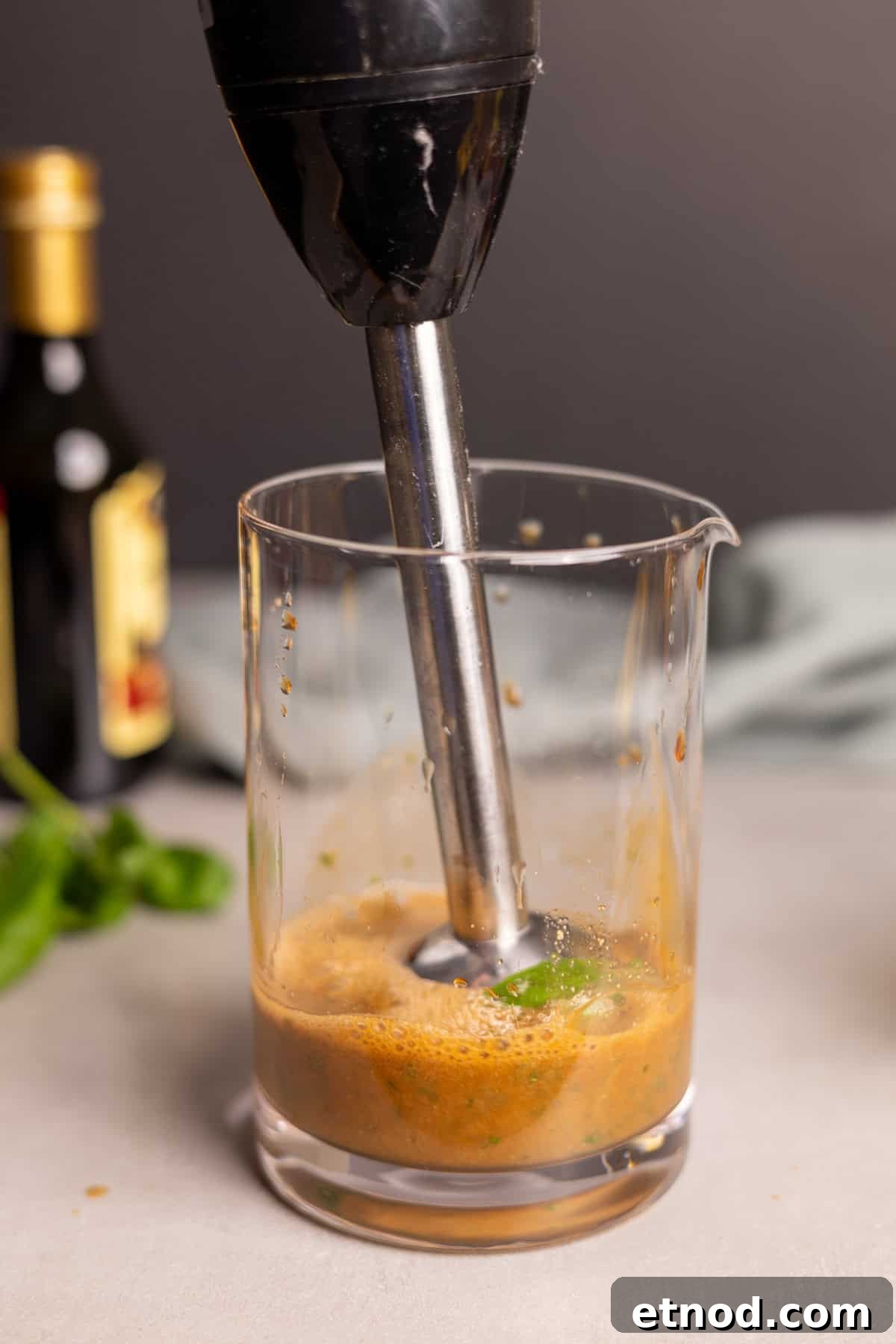 Ingredients for basil balsamic vinaigrette in a glass jar with an immersion blender mixing up the ingredients.