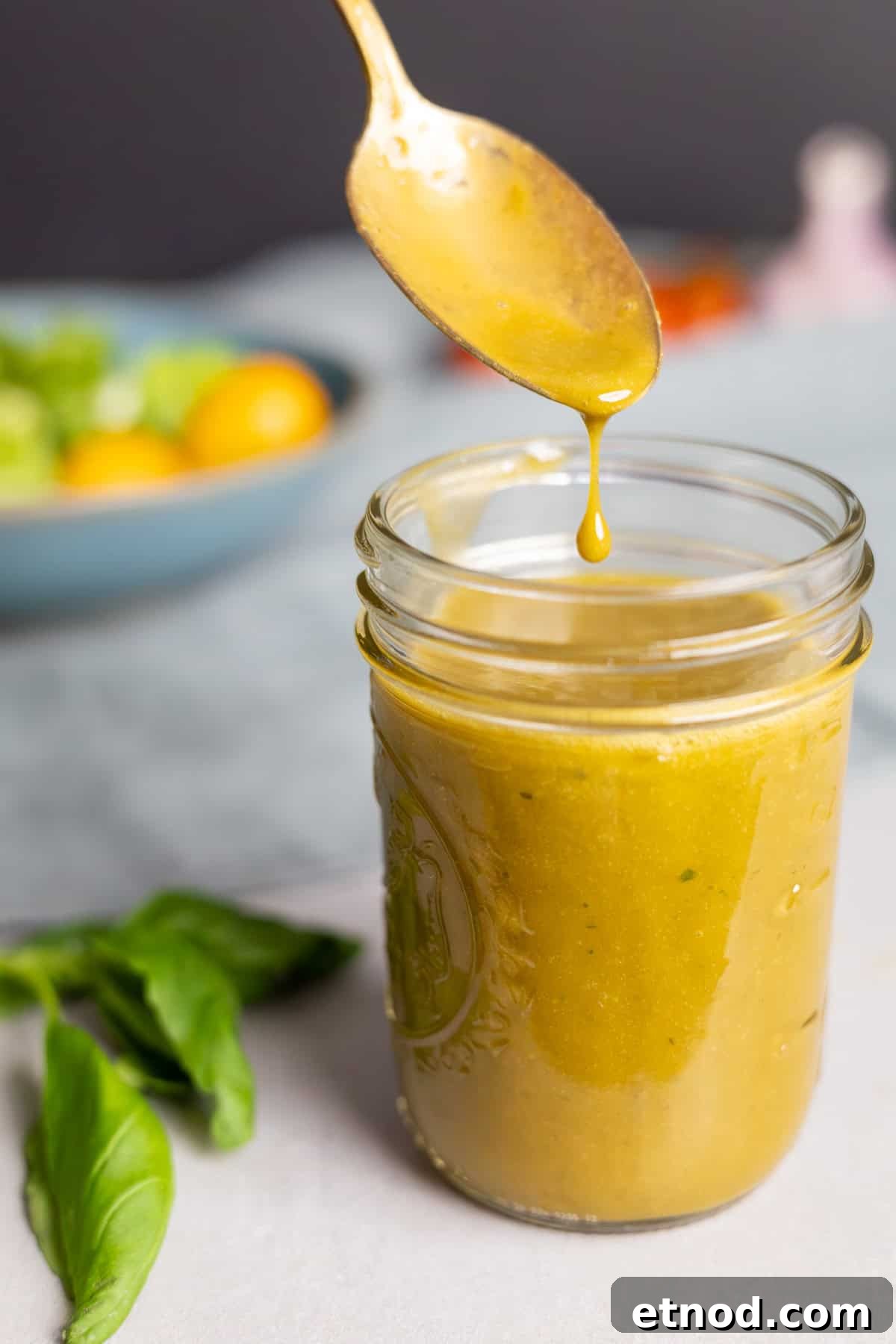 A spoon dripping creamy basil balsamic vinaigrette into a mason jar.