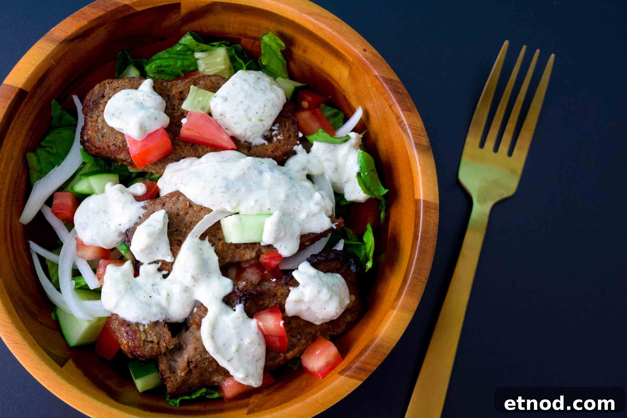 How to Make Authentic Gyro Meat at Home 5 Gyro meat in salad bowl covered in tzatziki sauce on black background