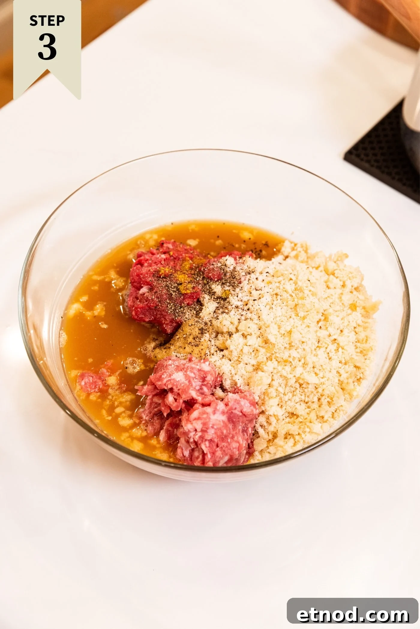 Classic Comfort Meatloaf Recipe for Perfect Weeknight Dinners 11 Glass bowl filled with all ingredients needed for meatloaf including ground meat, liquids, breadcrumbs, ketchup, and more sitting on white countertop.