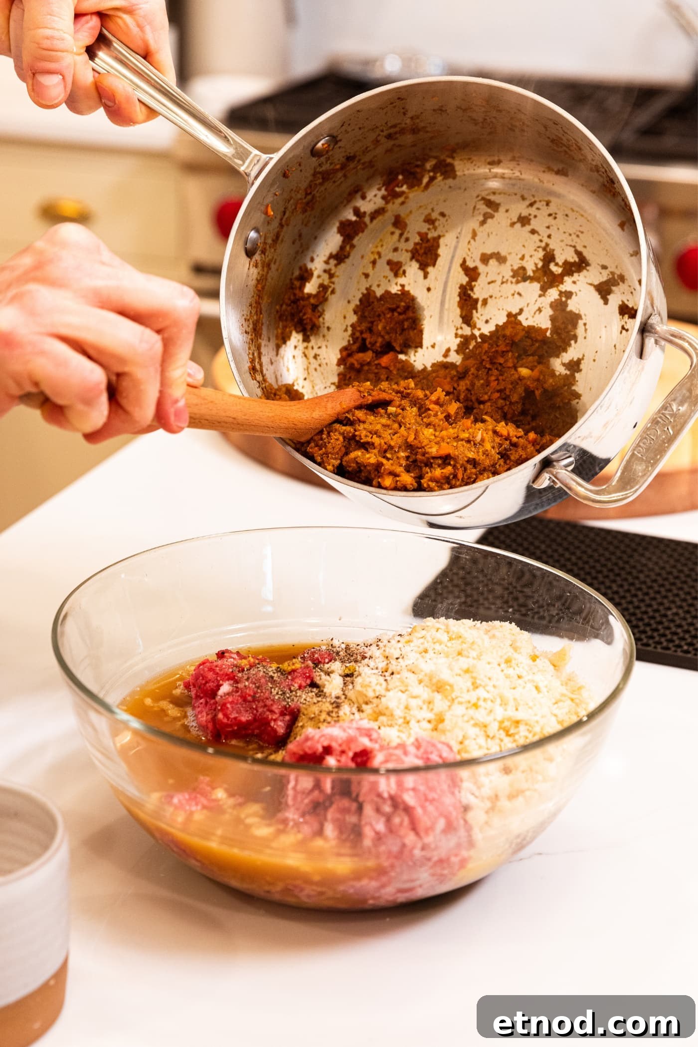 Classic Comfort Meatloaf Recipe for Perfect Weeknight Dinners 12 Hand scooping out vegetable mixture from metal stockpot with wooden spoon on top of glass bowl filled with meatloaf ingredients.