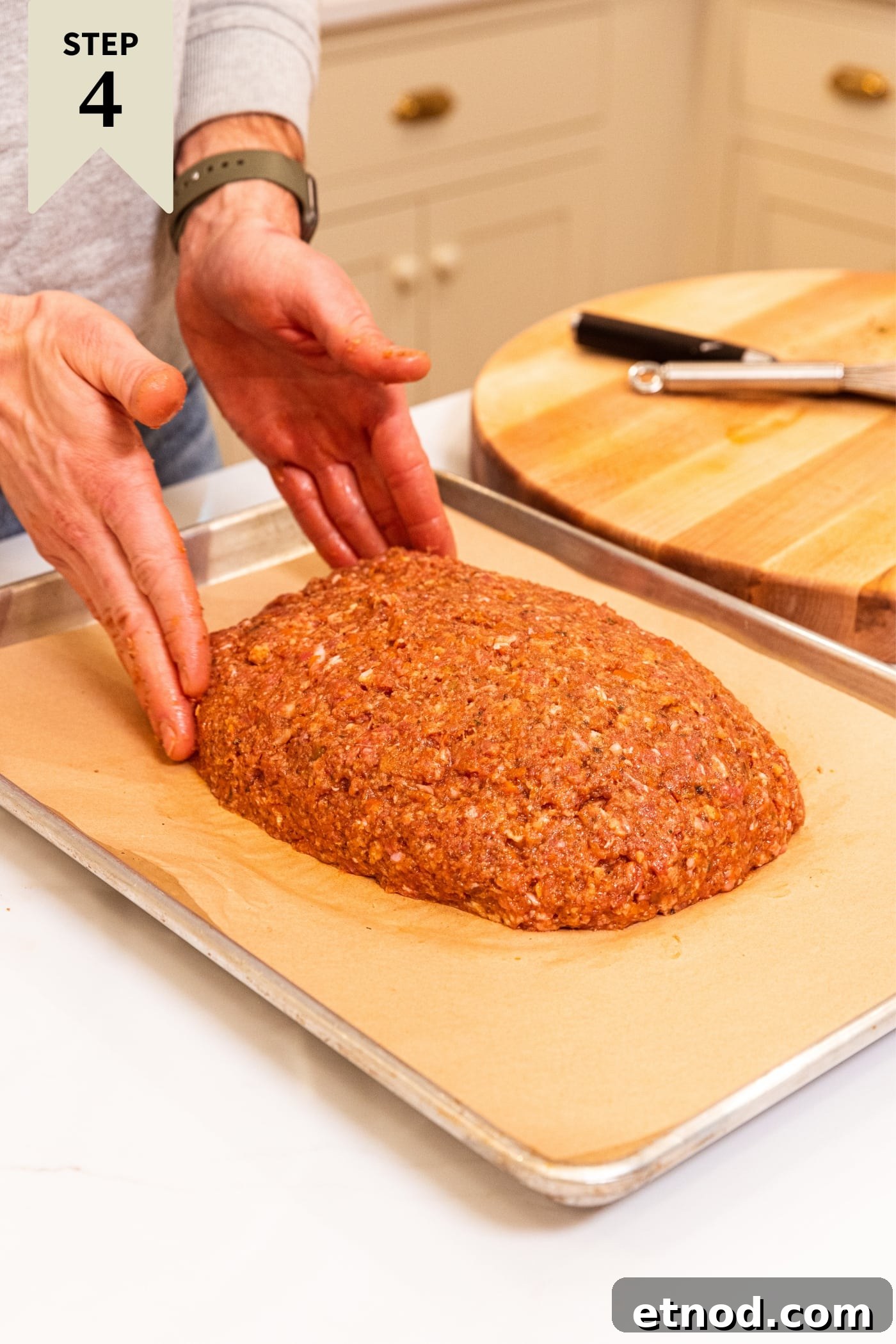 Classic Comfort Meatloaf Recipe for Perfect Weeknight Dinners 15 Two hands shaping meatloaf on parchment-lined baking sheet with wood cutting board in background.