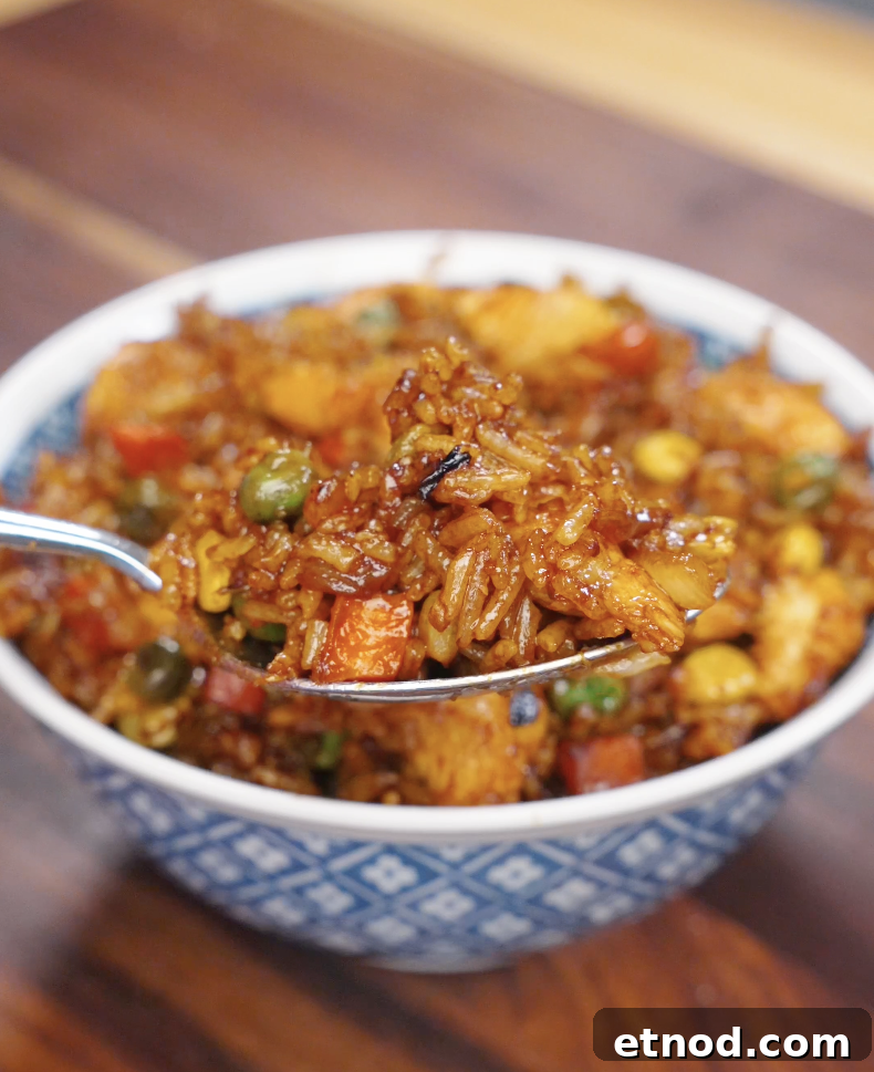 Spoon lifting chicken fried rice from a bowl, showing fluffy grains of rice mixed with chicken and vegetables.