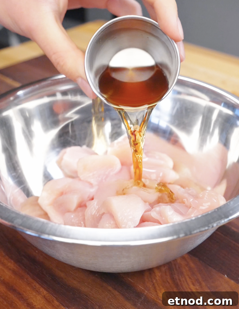 Shaoxing wine being poured over cubed raw chicken in a bowl, marinating the chicken for fried rice.