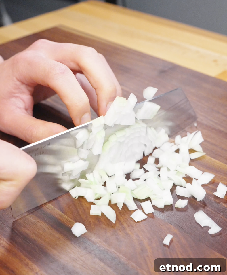 Onion being finely diced on a wooden cutting board, preparing aromatics for chicken fried rice.