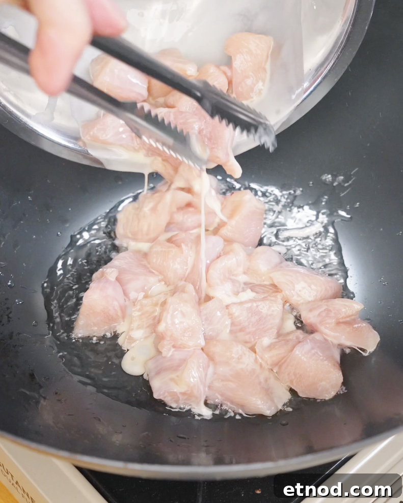 Marinated chicken pieces being placed into a hot pan with oil, starting the cooking process for chicken fried rice.