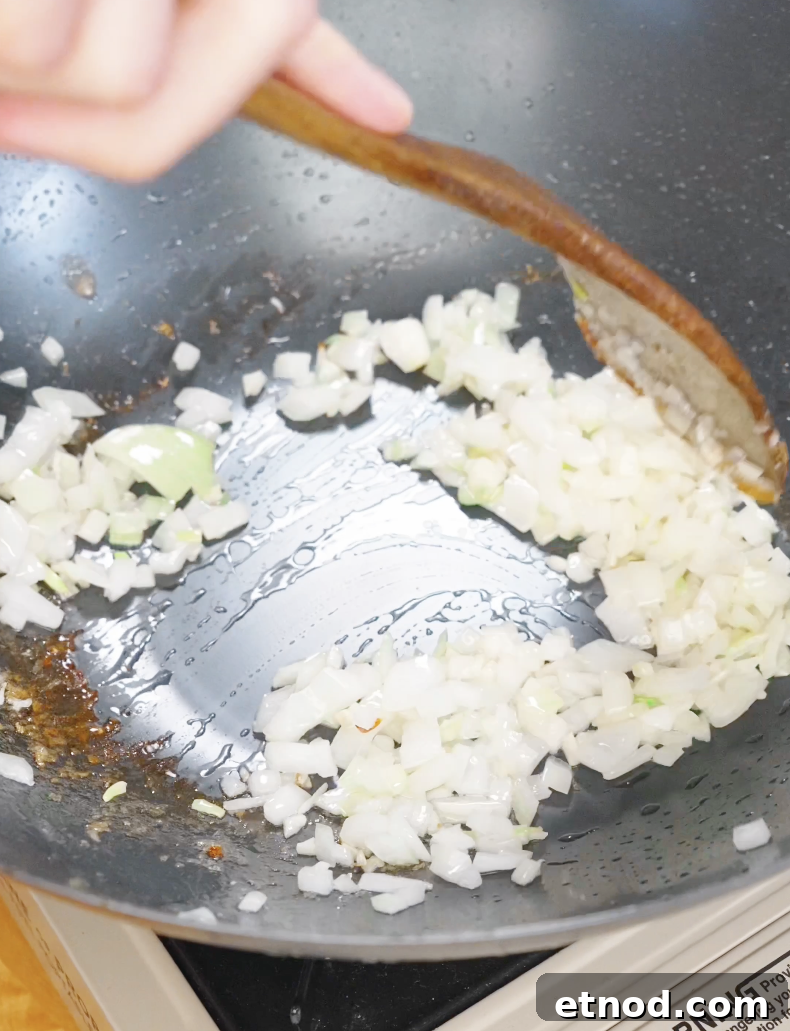 Finely diced onions being sautéed in a pan with oil, building the aromatic base for chicken fried rice.