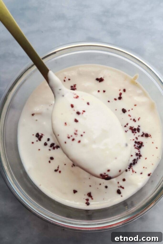 Roasted Garlic Butter Recipe: Creamy Spread for Bread & Cooking 13 Yogurt tahini sauce in a small glass bowl with a gold spoon coming out of it .