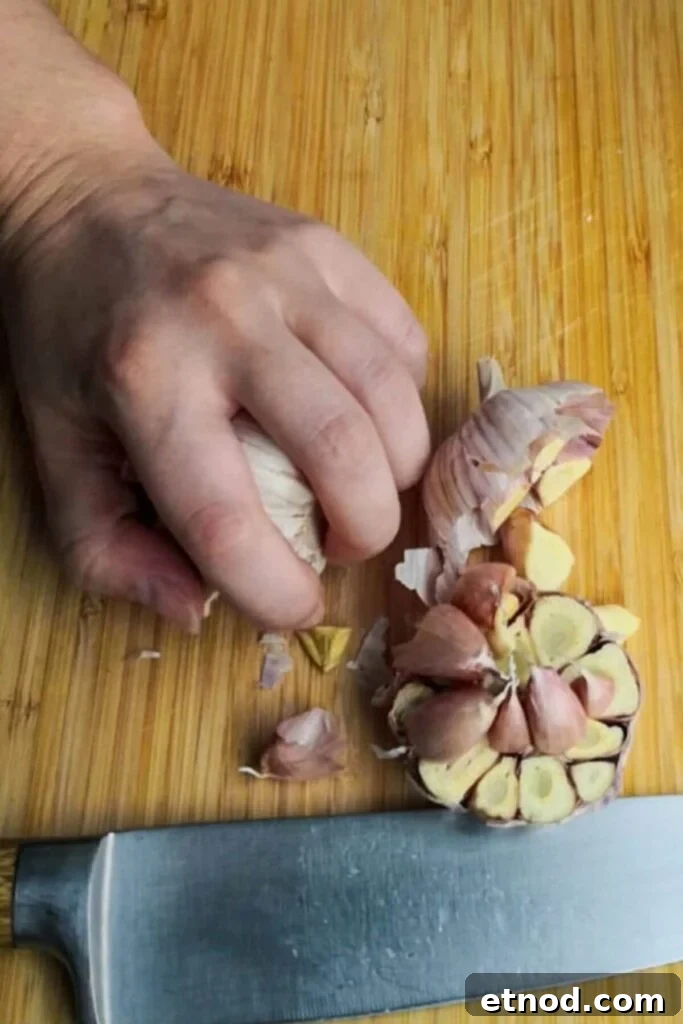 Roasted Garlic Butter Recipe: Creamy Spread for Bread & Cooking 4 Whole head of garlic cut in half on a wooden board, with a hand holding the other side of the garlic.