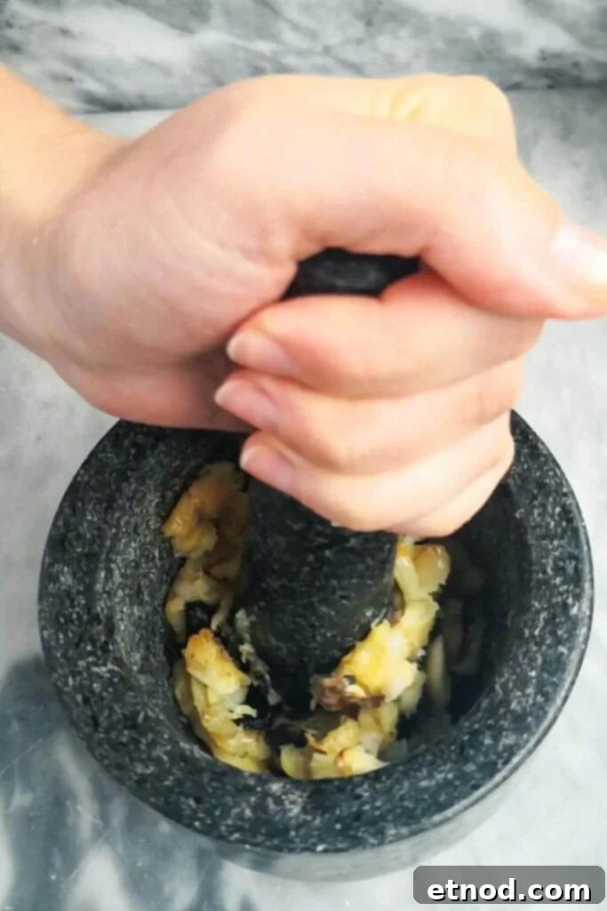 Roasted Garlic Butter Recipe: Creamy Spread for Bread & Cooking 7 Hand mashing roasted garlic into a paste in a pestle and mortar.