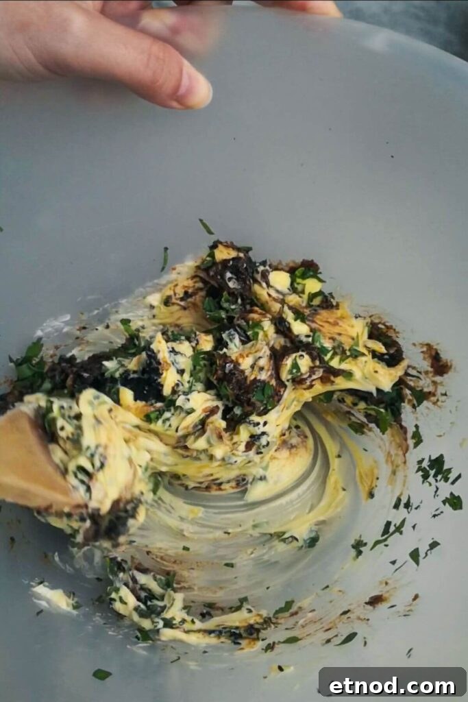 Roasted Garlic Butter Recipe: Creamy Spread for Bread & Cooking 8 Large wooden spoon starting to mix the roasted garlic butter in a large mixing bowl.