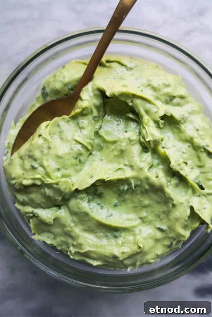 Roasted Garlic Butter Recipe: Creamy Spread for Bread & Cooking 10 Green tahini sauce in a small glass bowl with a gold spoon inside, on a grey marble background.