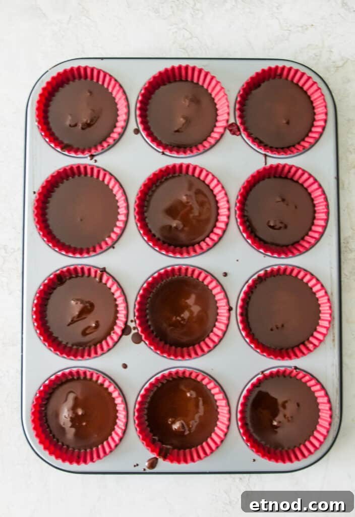High-Protein Raspberry-Filled Chocolate Truffles 11 A muffin pan lined with silicone muffin cups and each cup is filled with melted chocolate.