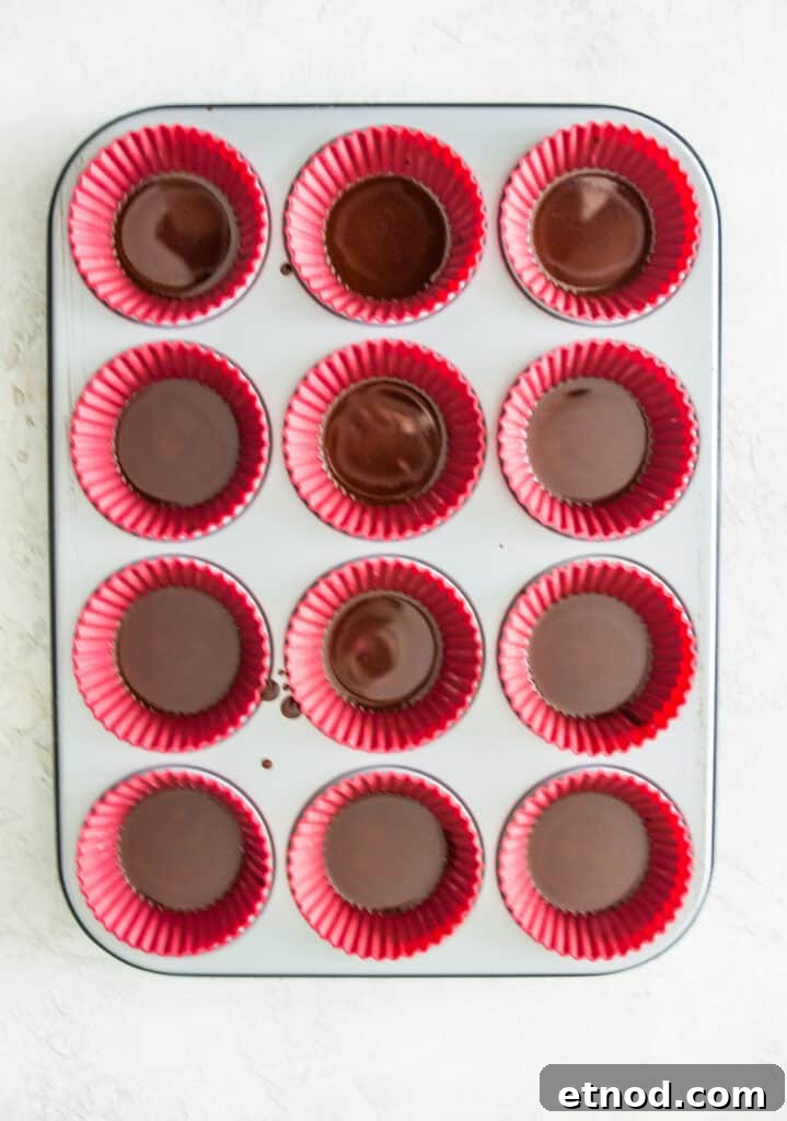 High-Protein Raspberry-Filled Chocolate Truffles 6 A muffin tray with silicone muffin liners in it with melted chocolate in each muffin cup.