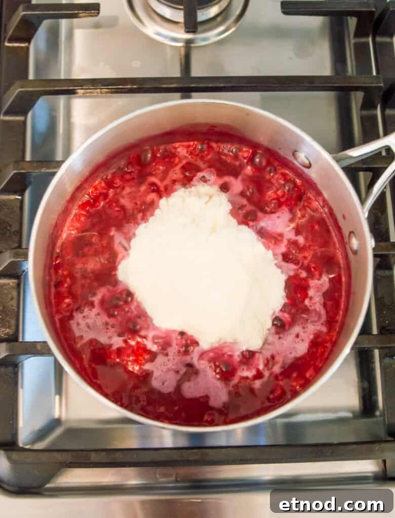 High-Protein Raspberry-Filled Chocolate Truffles 9 A pot on the stovetop filled with cooked raspberries with collagen powder on top of the raspberries.