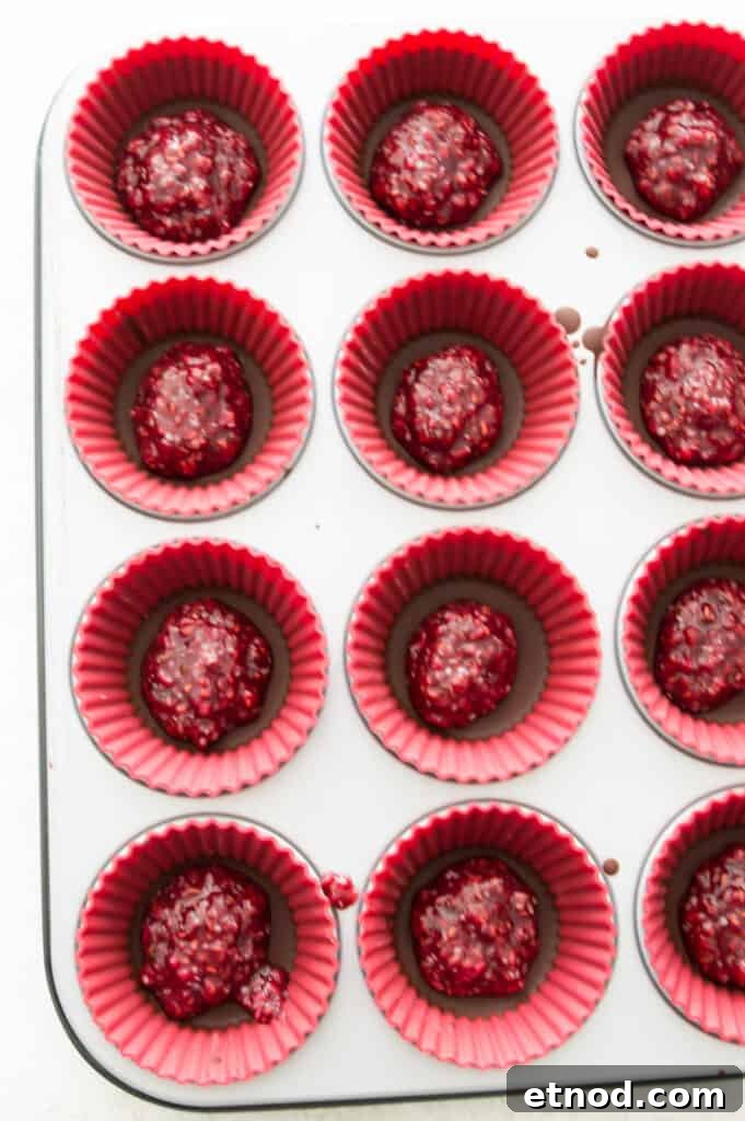 High-Protein Raspberry-Filled Chocolate Truffles 10 A muffin pan with silicone muffin cups in it with each cup filled with a raspberry mixture and chocolate.
