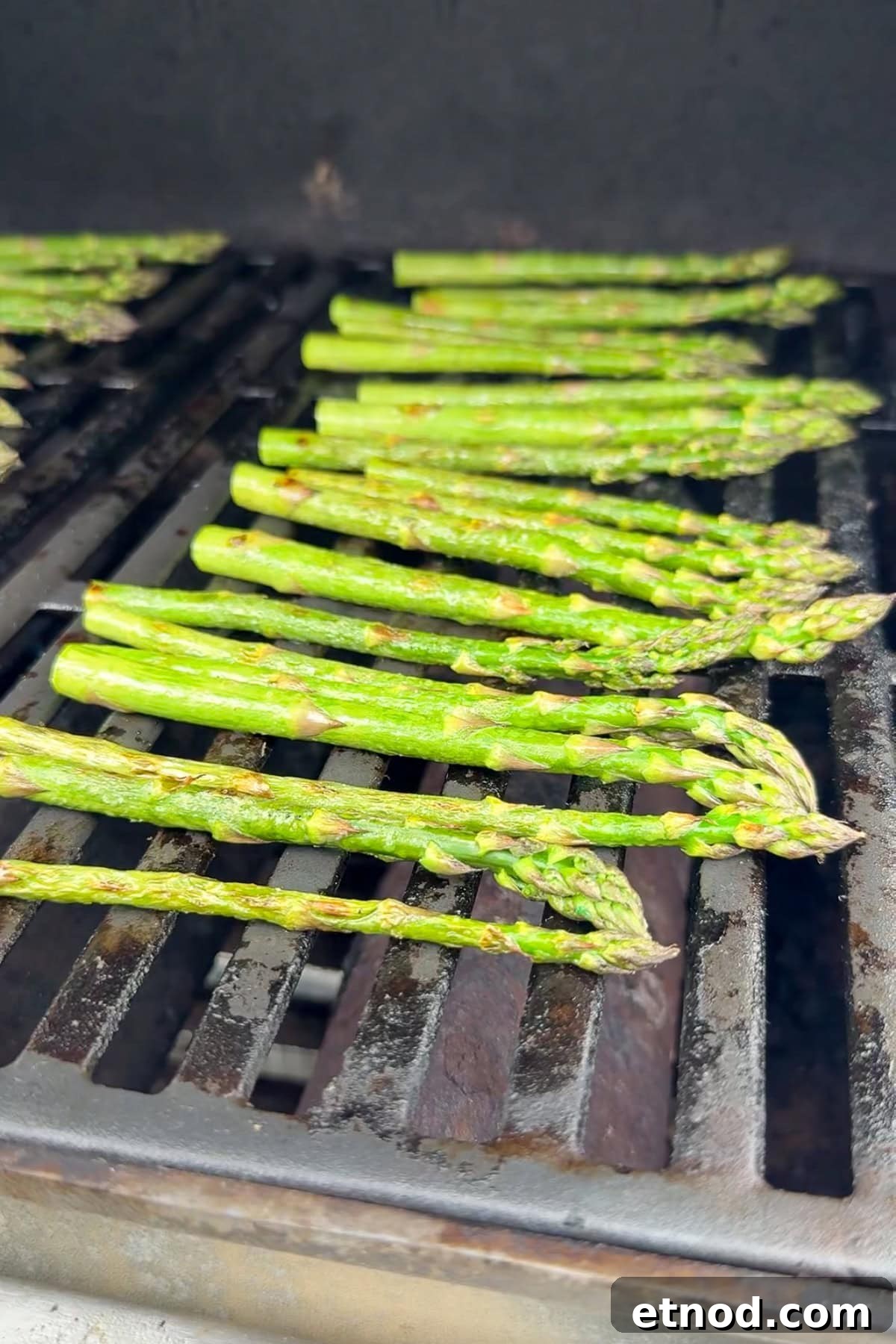 Grilled Asparagus Without Foil: Simple, Crispy Recipe Under 20 Minutes 2 Several stalks of asparagus are lined up and being grilled on the grates of a barbecue grill. The asparagus appears fresh and is beginning to show slight char marks.