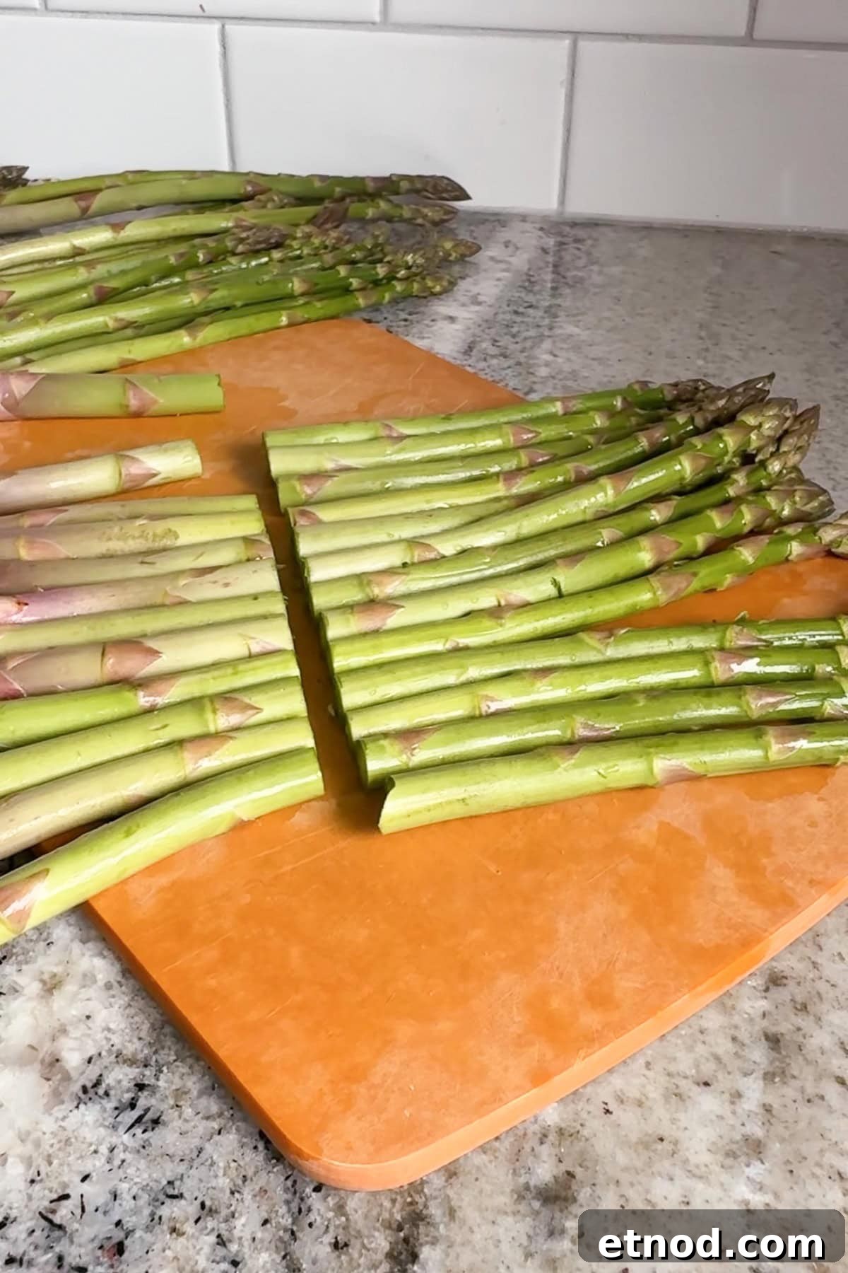 Grilled Asparagus Without Foil: Simple, Crispy Recipe Under 20 Minutes 5 Fresh asparagus spears are arranged in rows on an orange cutting board, with more asparagus in the background on a granite countertop.