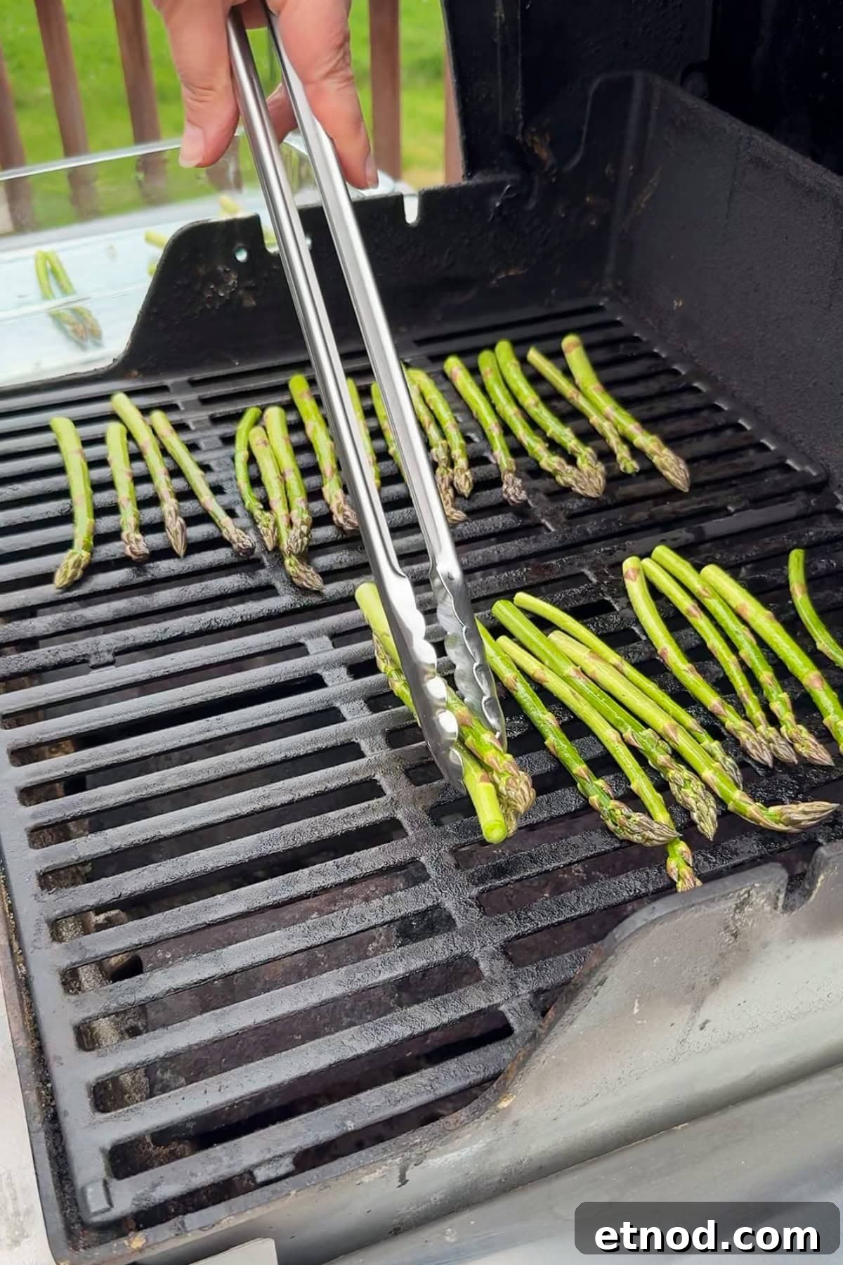 Grilled Asparagus Without Foil: Simple, Crispy Recipe Under 20 Minutes 7 A person uses metal tongs to grill asparagus spears on a black outdoor grill. The asparagus is arranged in rows across the grill grates.