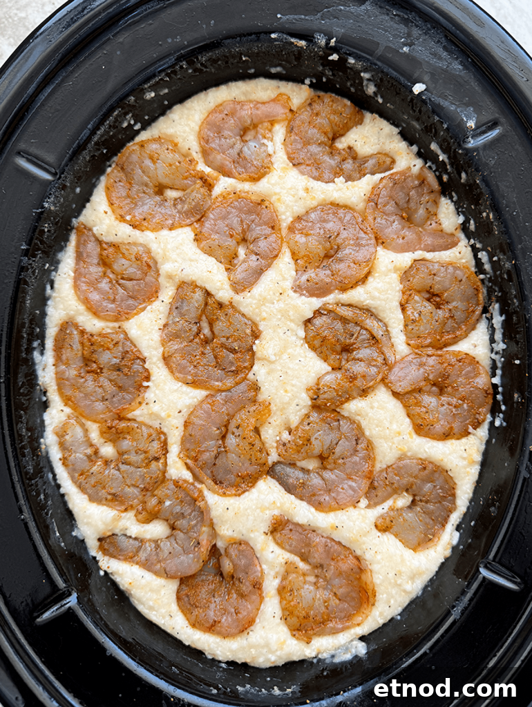 overhead shot of cooked grits with uncooked shrimp in a black slow cooker