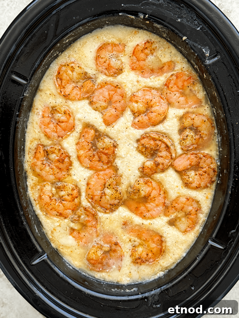 overhead shot of cooked grits with cooked shrimp in a black slow cooker