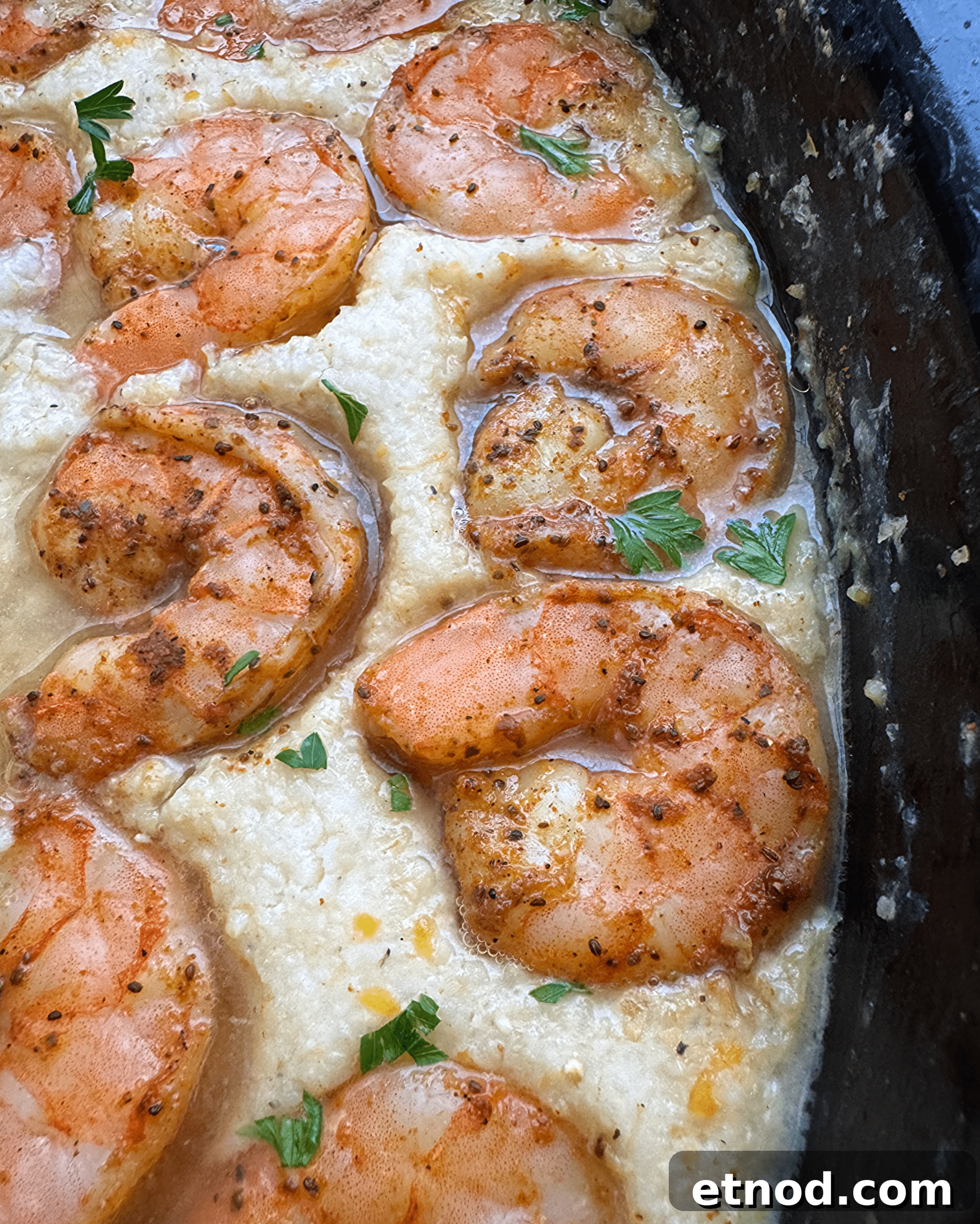 Creamy Slow Cooker Shrimp and Grits Recipe 7 close up shot of cooked shrimp and grits in a black slow cooker garnished with fresh parsley