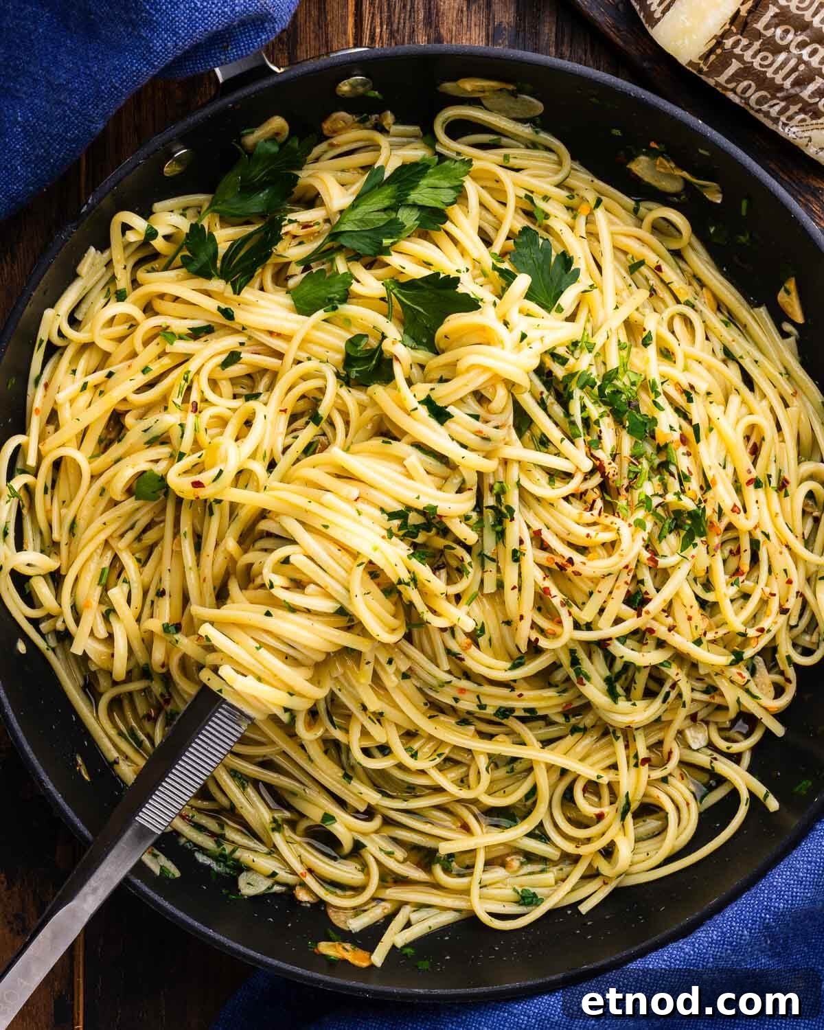 Linguine aglio e olio in large black pan with kitchen tweezers.