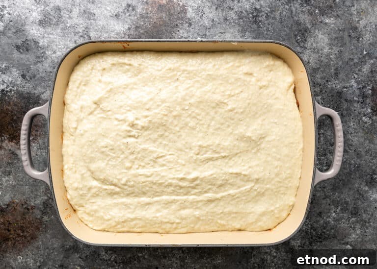 Authentic Greek Pastitsio Recipe: Classic Baked Pasta with Bechamel 12 overhead process shot: layer of bechamel sauce in baking dish for greek lasagna