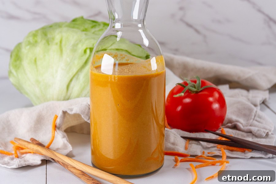 a bottle of salad dressing in front of a head of lettuce and a tomato.