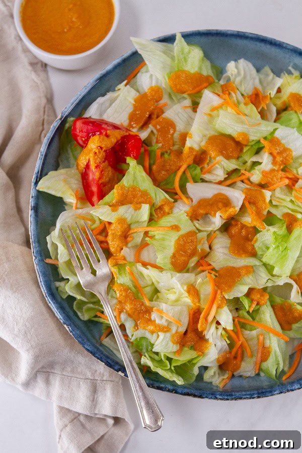 a large blue bowl filled with salad and a fork in the bowl, a small bowl of dressing in the upper left.