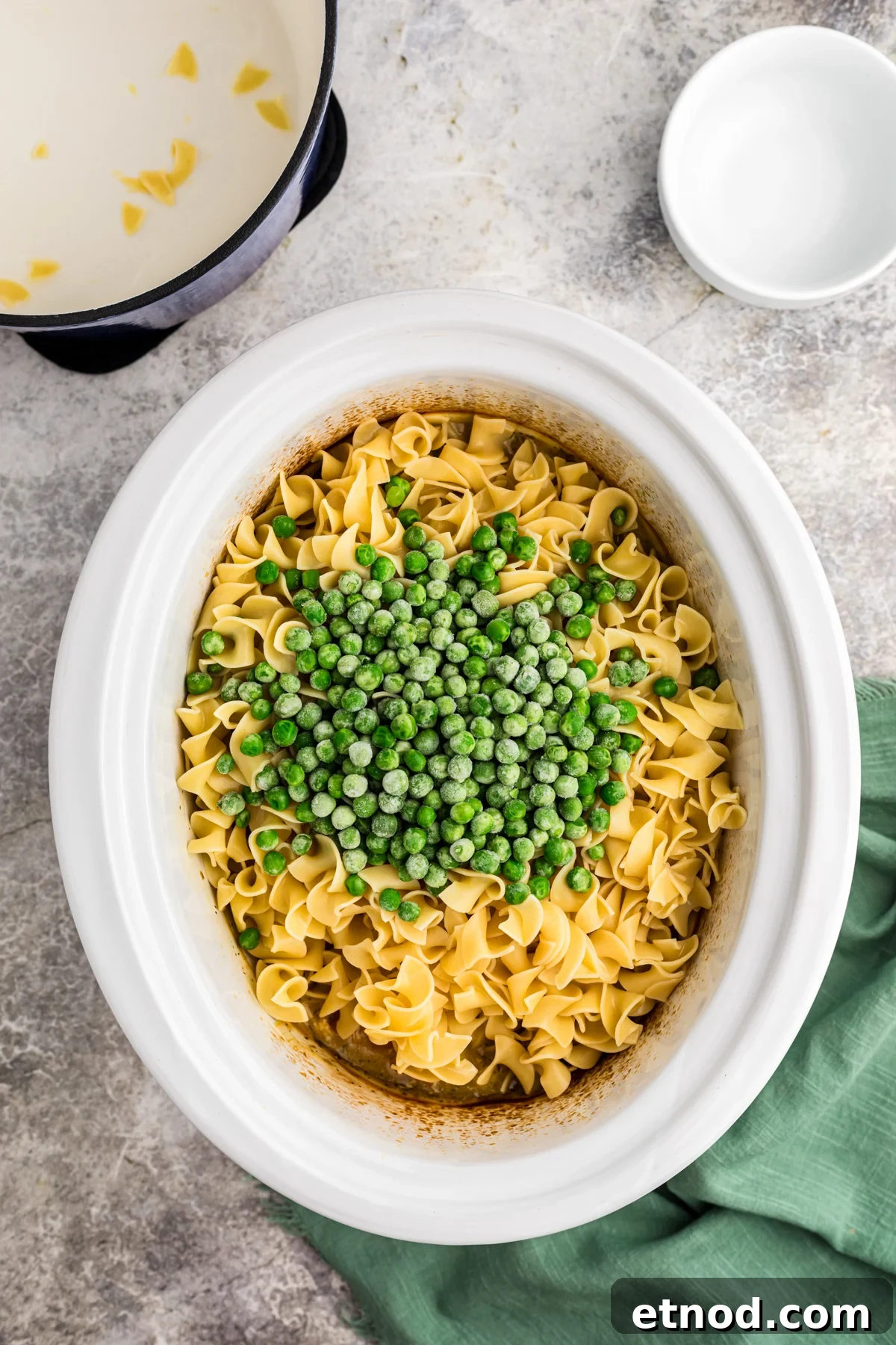 Creamy Slow Cooker Chicken and Noodles Recipe 6 egg noodles, peas on top of chicken and sauce in a slow cooker.