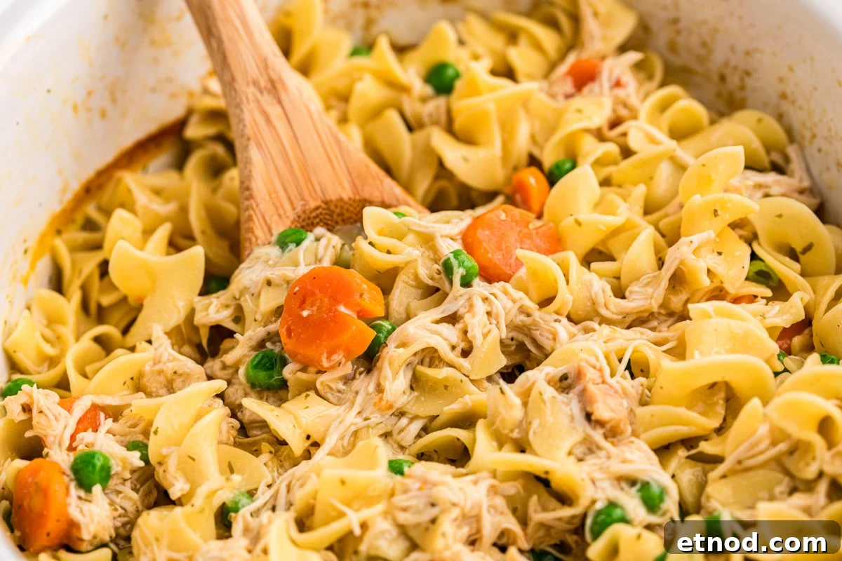 Creamy Slow Cooker Chicken and Noodles Recipe 8 Close up of chicken and noodles in a slow cooker with a wooden spoon in it.