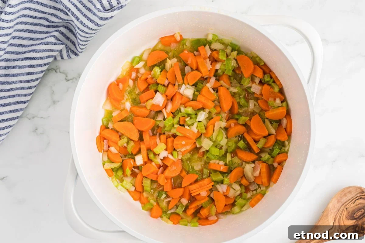 Creamy Homemade Chicken Noodle Soup Recipe for Comforting Dinner 4 chopped carrots, celery, and onion sautéing in a Dutch oven.