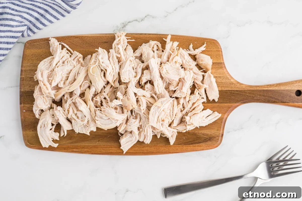 Creamy Homemade Chicken Noodle Soup Recipe for Comforting Dinner 7 shredded cooked chicken on a wooden cutting board, with two forks on side.