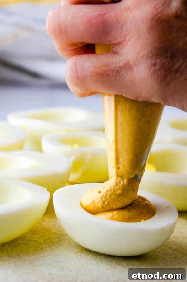 Southern-Style Deviled Eggs Recipe: Tangy Classic Appetizer 5 piping spicy egg yolk filling into the deviled eggs.