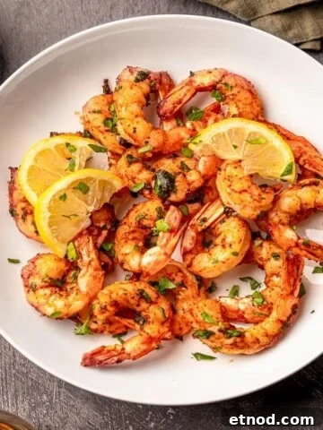 A white bowl filled with shrimp topped with lemon slices nest to a green napkin.