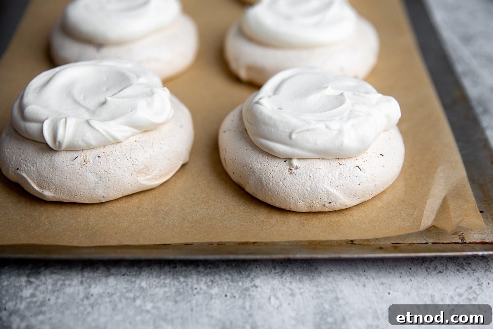 Mini pavlovas topped with whipped cream on a baking sheet.